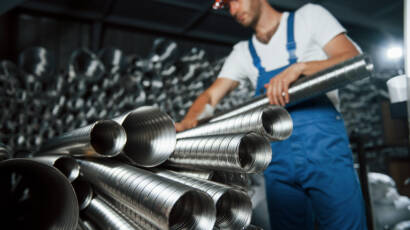 Silver colored ventilation pipes. Man in uniform works on the production. Industrial modern technology.