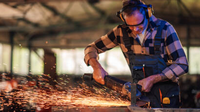 Young expert in the workshop carefully grinding metal while shaping it to perfection and creating sturdy structures of the construction. Dedicated work in a dangerous environment. Wearing safety gear.